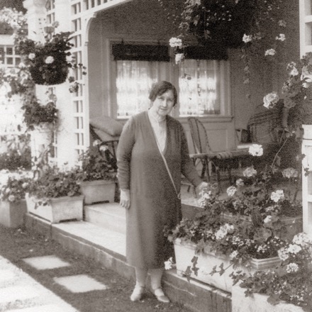 Jennie Butchart se trouve au centre de la première photographie en noir et blanc. Elle pose devant sa résidence où l’on voit plusieurs jardinières. Quelques-unes sont suspendues à un treillis; d’autres embellissent le sol. Elles sont toutes garnies de plantes de tailles et de floraisons distinctes.